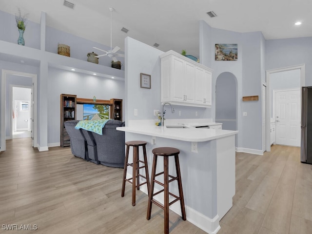 kitchen featuring kitchen peninsula, sink, light hardwood / wood-style flooring, white cabinets, and a breakfast bar area