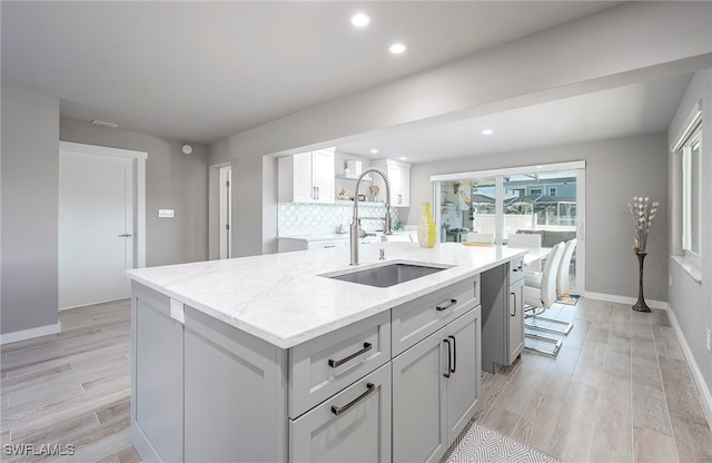 kitchen with sink, light wood-type flooring, light stone countertops, and a center island with sink