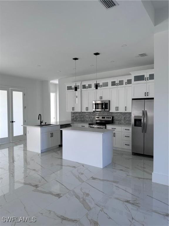 kitchen featuring white cabinetry, a center island, backsplash, decorative light fixtures, and appliances with stainless steel finishes