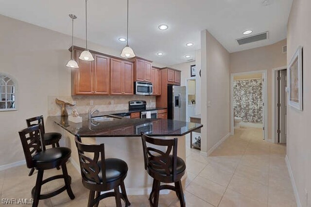 kitchen featuring appliances with stainless steel finishes, a kitchen bar, tasteful backsplash, hanging light fixtures, and kitchen peninsula