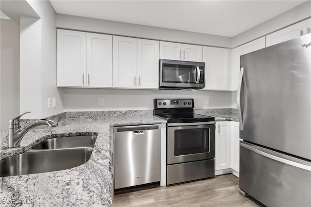 kitchen featuring sink, light hardwood / wood-style flooring, appliances with stainless steel finishes, white cabinetry, and light stone countertops