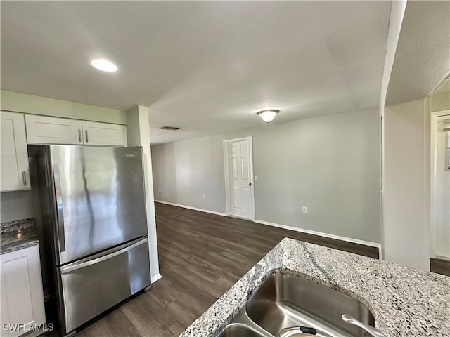 kitchen featuring stainless steel refrigerator, dark wood-type flooring, light stone counters, and white cabinets