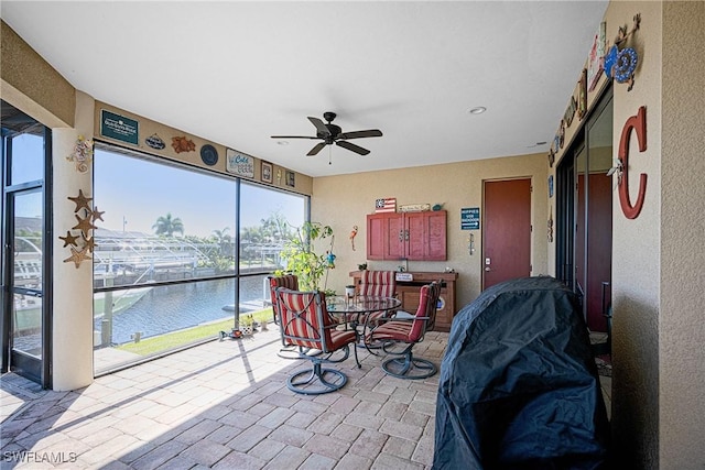 sunroom with ceiling fan and a water view