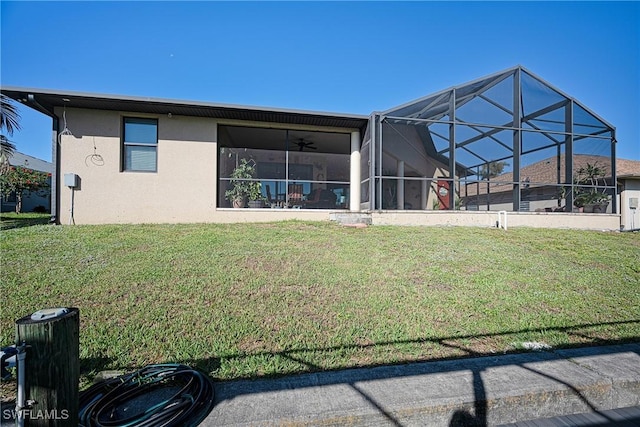 back of property featuring glass enclosure, ceiling fan, and a lawn