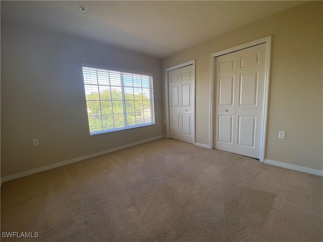 unfurnished bedroom with light carpet and multiple closets