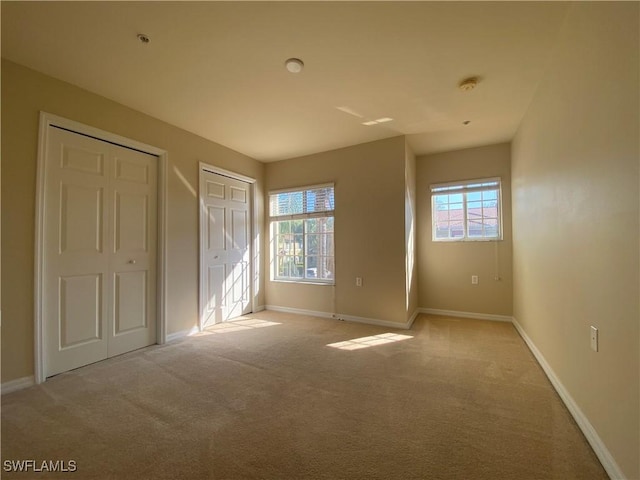 unfurnished bedroom with multiple closets and light colored carpet