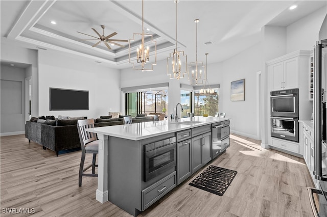 kitchen with gray cabinetry, hanging light fixtures, a kitchen breakfast bar, an island with sink, and light wood-type flooring