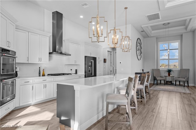 kitchen with a center island with sink, a kitchen breakfast bar, wall chimney range hood, appliances with stainless steel finishes, and decorative light fixtures