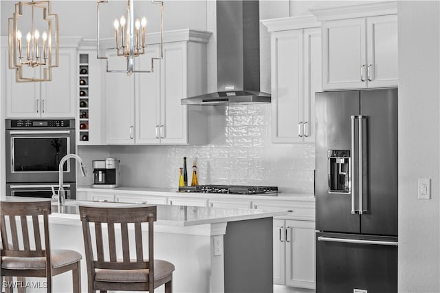 kitchen featuring a center island with sink, wall chimney exhaust hood, decorative light fixtures, white cabinetry, and stainless steel appliances