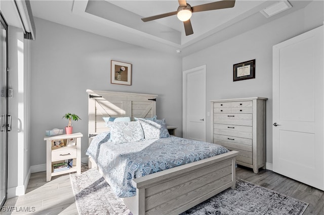 bedroom with a tray ceiling, ceiling fan, and light wood-type flooring