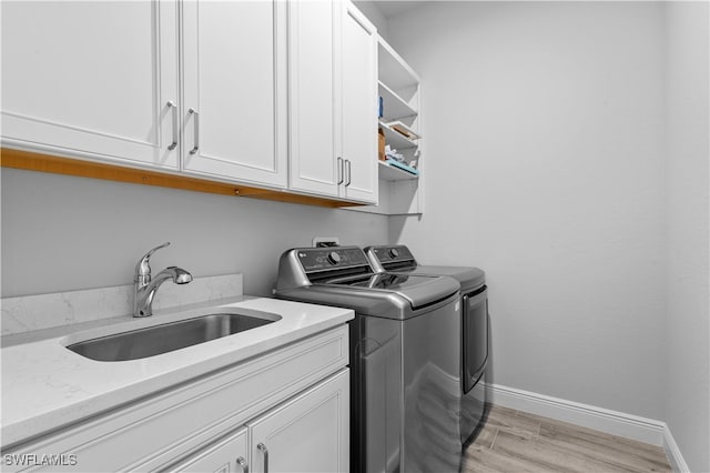 clothes washing area with washer and dryer, cabinets, sink, and light hardwood / wood-style flooring