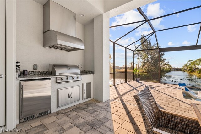 view of patio featuring grilling area, a water view, exterior kitchen, and glass enclosure