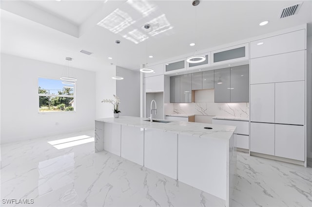 kitchen with backsplash, sink, a center island with sink, gray cabinets, and hanging light fixtures