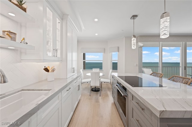 kitchen with tasteful backsplash, a water view, light hardwood / wood-style flooring, white cabinetry, and hanging light fixtures