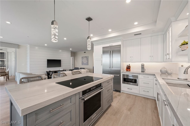 kitchen with built in appliances, white cabinets, light stone counters, and hanging light fixtures