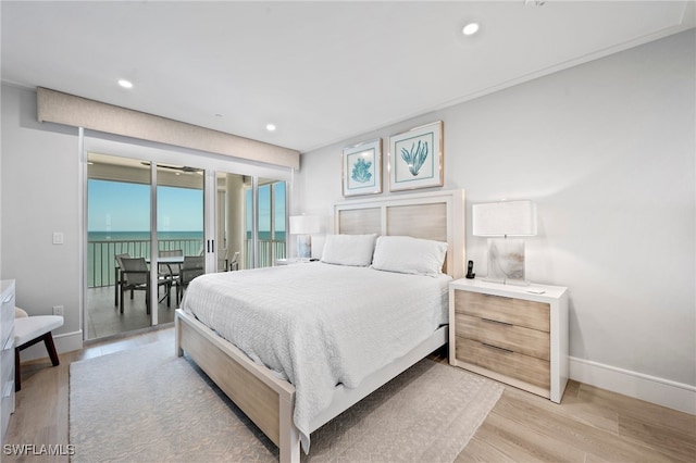 bedroom featuring access to outside, light hardwood / wood-style flooring, and a water view