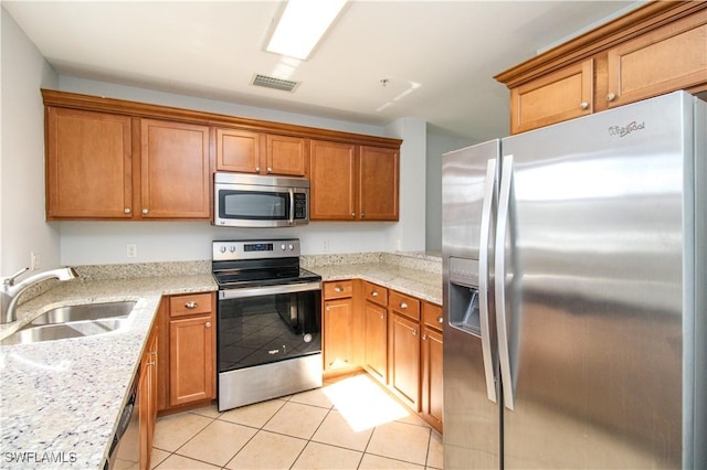 kitchen with sink, light tile patterned flooring, light stone counters, and stainless steel appliances