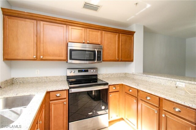 kitchen with stainless steel appliances, light stone counters, and sink