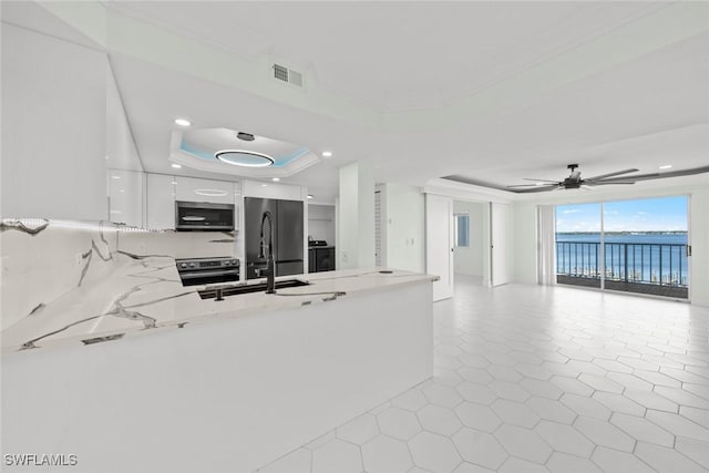 kitchen with white cabinets, a raised ceiling, a water view, built in refrigerator, and ceiling fan