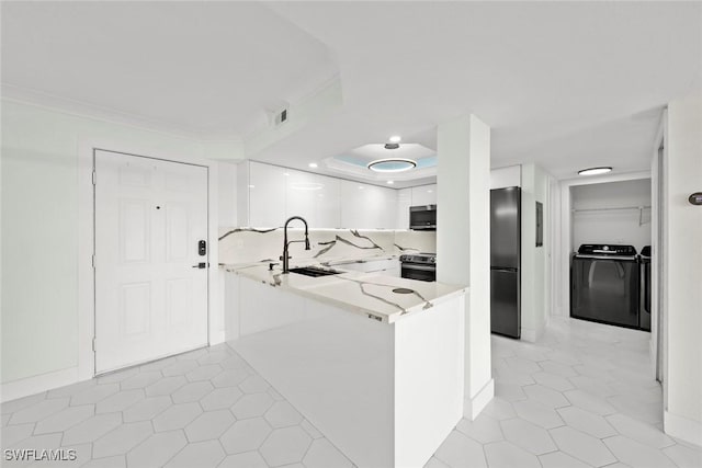 kitchen with washer and clothes dryer, sink, kitchen peninsula, appliances with stainless steel finishes, and white cabinetry