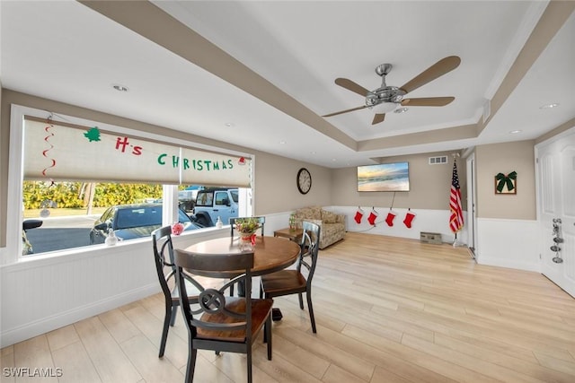 dining area featuring a raised ceiling, ceiling fan, and light hardwood / wood-style flooring