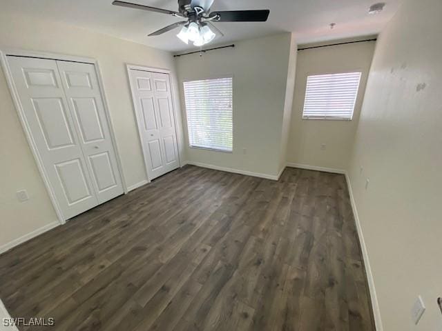 unfurnished bedroom with ceiling fan, dark hardwood / wood-style flooring, and two closets