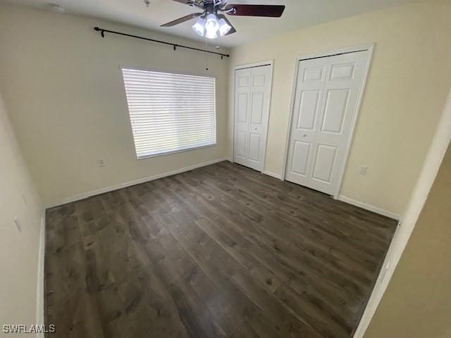 unfurnished bedroom featuring ceiling fan, dark hardwood / wood-style flooring, and two closets