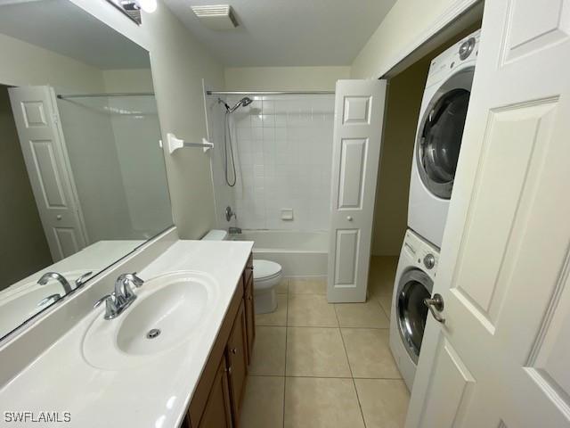 full bathroom featuring vanity, stacked washer and dryer, tiled shower / bath, tile patterned flooring, and toilet