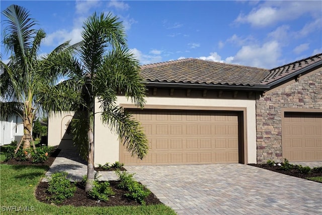 view of front of home with a garage, stone siding, decorative driveway, and stucco siding