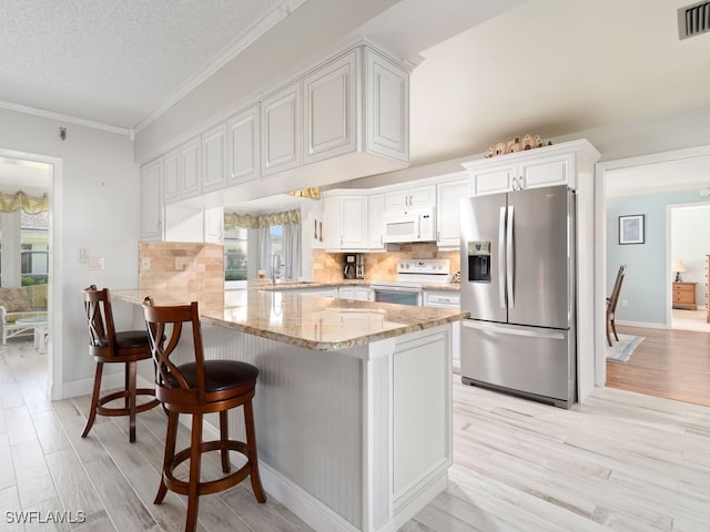 kitchen featuring kitchen peninsula, white appliances, white cabinetry, and a wealth of natural light