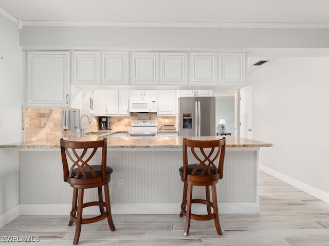 kitchen featuring white cabinetry, a kitchen bar, white appliances, and light stone counters