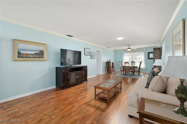 living room featuring ceiling fan, wood-type flooring, a textured ceiling, and ornamental molding