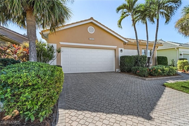 ranch-style home featuring decorative driveway, a tiled roof, an attached garage, and stucco siding