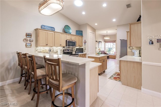 kitchen with stainless steel appliances, decorative backsplash, a kitchen bar, and kitchen peninsula