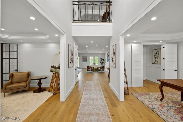 entryway with light wood-type flooring, a tray ceiling, and ornamental molding