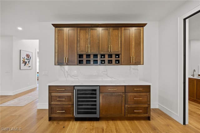 bar featuring tasteful backsplash, wine cooler, light stone counters, and light hardwood / wood-style floors