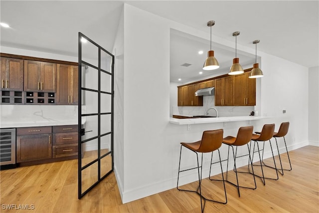 55 E Burning Tree Dr, Naples, FL 34105 - kitchen with under cabinet range hood, beverage cooler, a kitchen breakfast bar, decorative backsplash, and light countertops