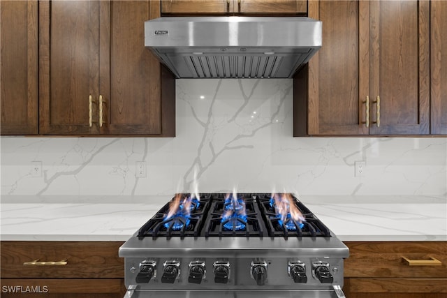 kitchen featuring light stone countertops, stainless steel stove, tasteful backsplash, and wall chimney range hood