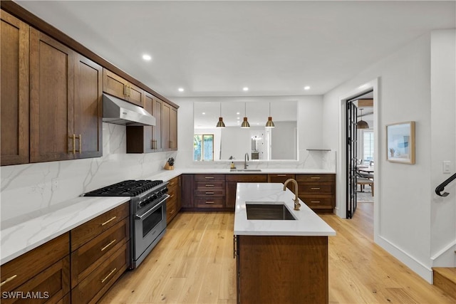 55 E Burning Tree Dr, Naples, FL 34105 - kitchen with under cabinet range hood, stainless steel stove, a sink, a center island with sink, and recessed lighting