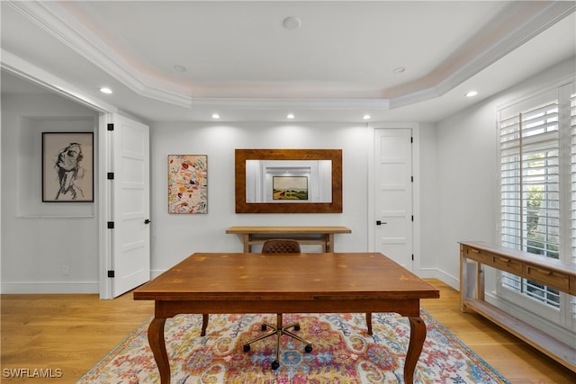 home office with a raised ceiling, ornamental molding, and light wood-type flooring