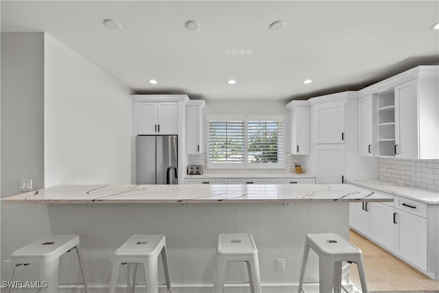 kitchen featuring light stone countertops, tasteful backsplash, stainless steel fridge, a breakfast bar, and white cabinets