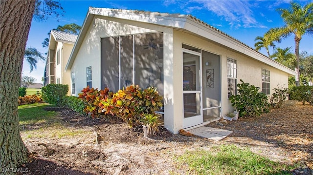 view of side of property featuring a sunroom, a tiled roof, and stucco siding