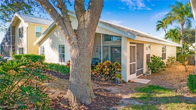 view of property exterior featuring a sunroom, a tile roof, and stucco siding