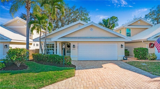 view of front facade featuring an attached garage, a front yard, decorative driveway, and stucco siding