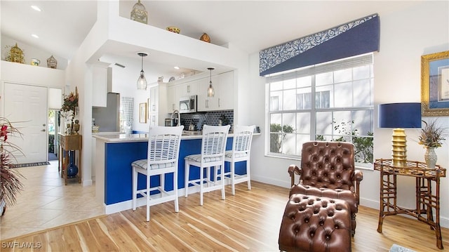 kitchen featuring white cabinets, pendant lighting, stainless steel appliances, and light hardwood / wood-style floors