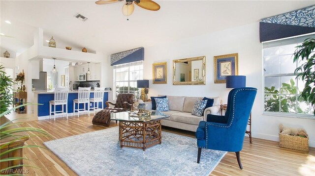 living room with ceiling fan, light hardwood / wood-style flooring, and vaulted ceiling