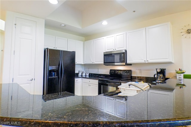 kitchen featuring a raised ceiling, dark stone countertops, white cabinetry, and black appliances