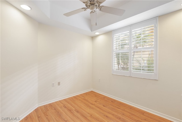 spare room with a raised ceiling, ceiling fan, and light hardwood / wood-style floors