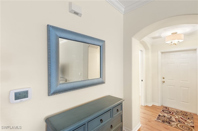 doorway with light wood-type flooring, baseboards, ornamental molding, and arched walkways