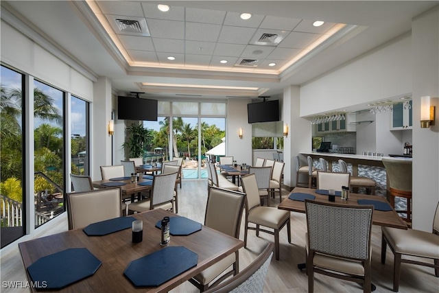 dining space featuring a tray ceiling, a wealth of natural light, light wood finished floors, and visible vents
